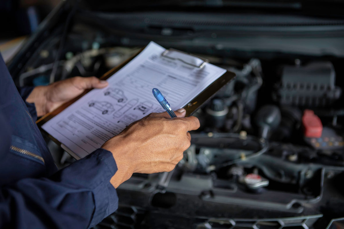 Hands holding clipboard next to car engine